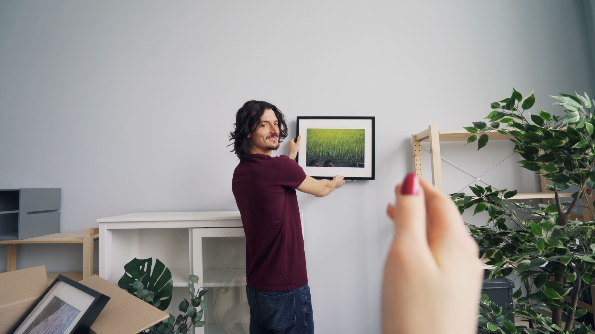 Handyman hanging a framed picture on the wall of a bright, plant-filled South Florida home