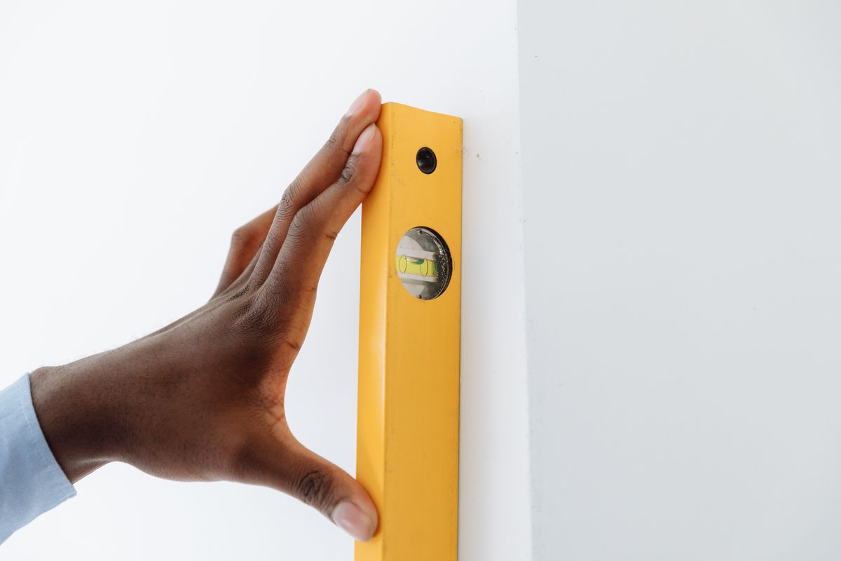 Hand using a yellow level to hang a shelf perfectly straight on a white wall